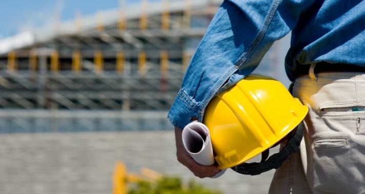 Trabajador de MMC con casco y planos de obra frente a una estructura en construcción